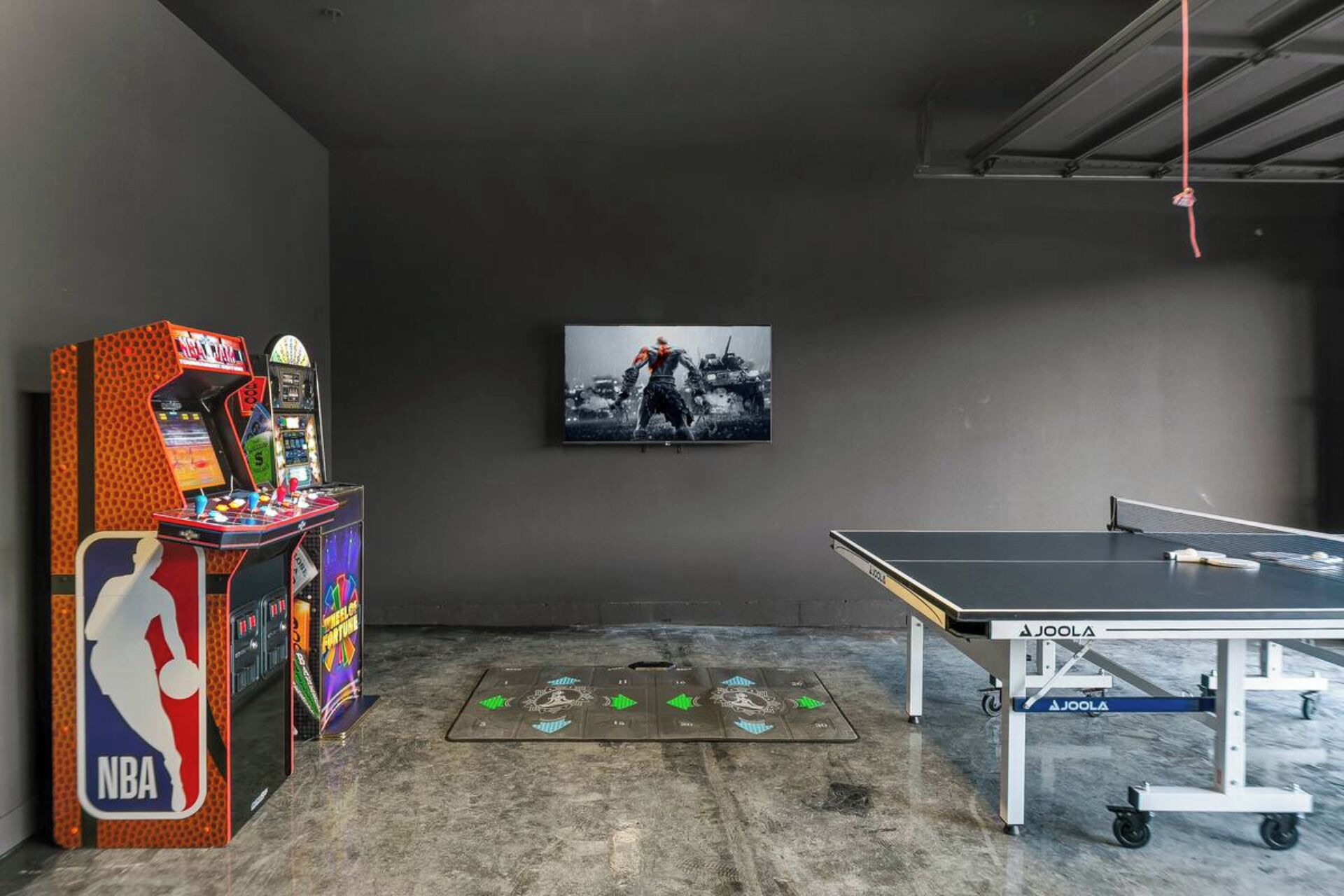 Une pièce avec une table de ping-pong, un jeu d’arcade de basket-ball et un tableau encadré accroché au mur.