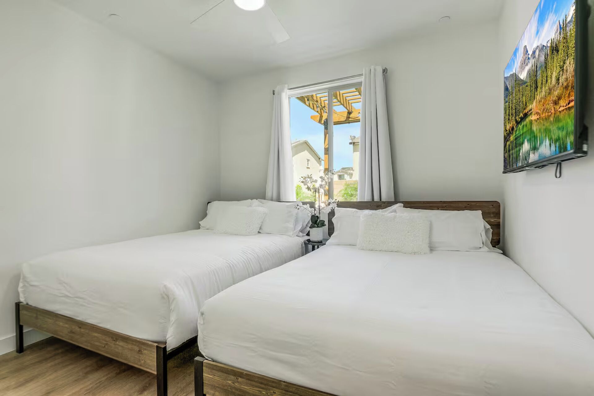 Un dormitorio con dos camas individuales, una ventana con cortinas, un ventilador de techo y un cuadro en la pared.