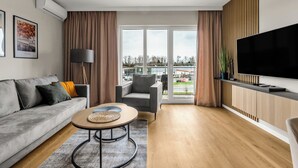 Un salon moderne avec un canapé gris, une table basse ronde, un téléviseur et une vue sur l’extérieur.