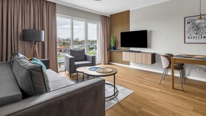 Un salon moderne avec un canapé gris, une table basse ronde, un téléviseur fixé au mur et un coin repas comprenant une table et des chaises en bois.