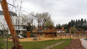 Une aire de jeux avec une cabane en bois, des balançoires et un toboggan.