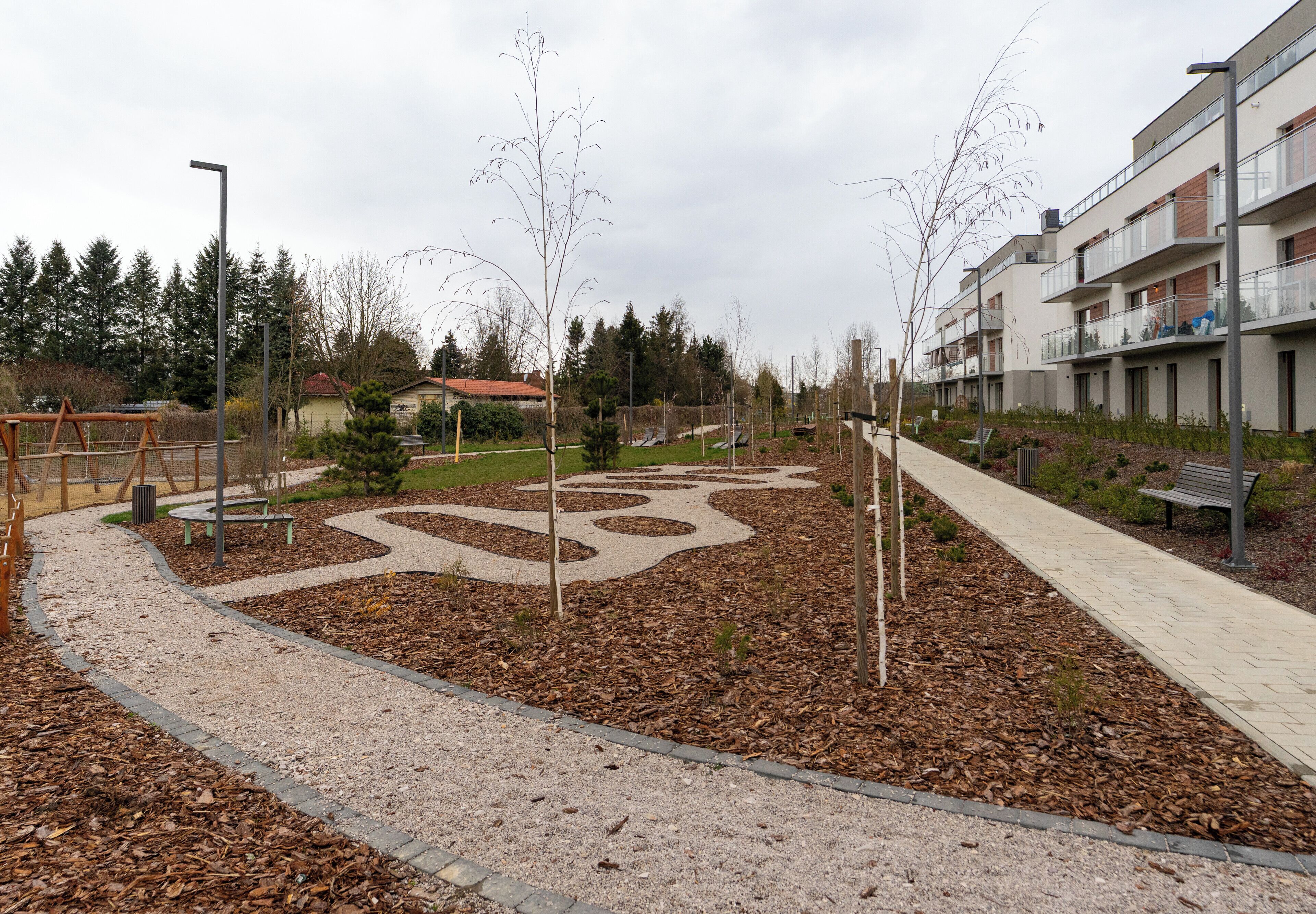 Un parc avec un sentier sinueux, des bancs et une aire de jeux.
