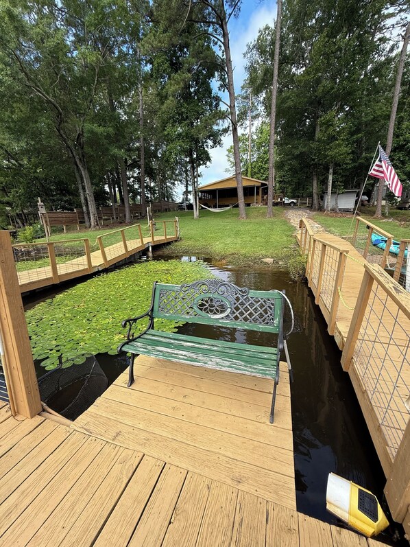 A wooden deck with a bench, a small pond with lily pads, and a wooden fence.