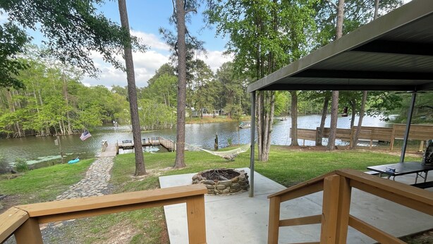 A wooden deck with a stone fire pit, a view of a lake with boats, and a covered picnic area.