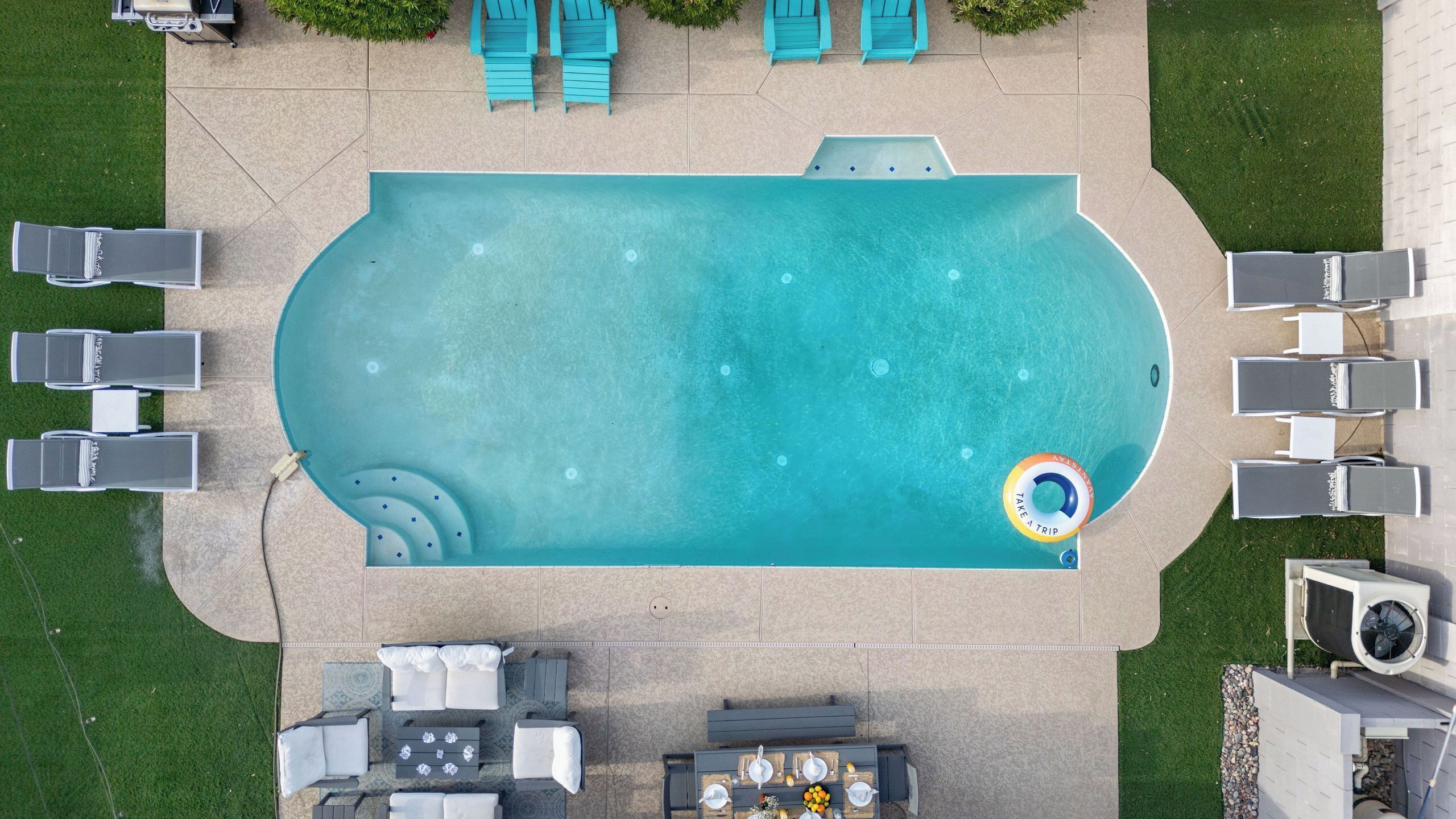 Eine Vogelperspektive auf einen Pool mit Liegestühlen, einem Essbereich und einem Wasserspiel.