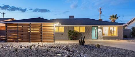 A modern house with a covered patio, a well-maintained garden with rocks and cacti, and a visible number '8022' on the door.