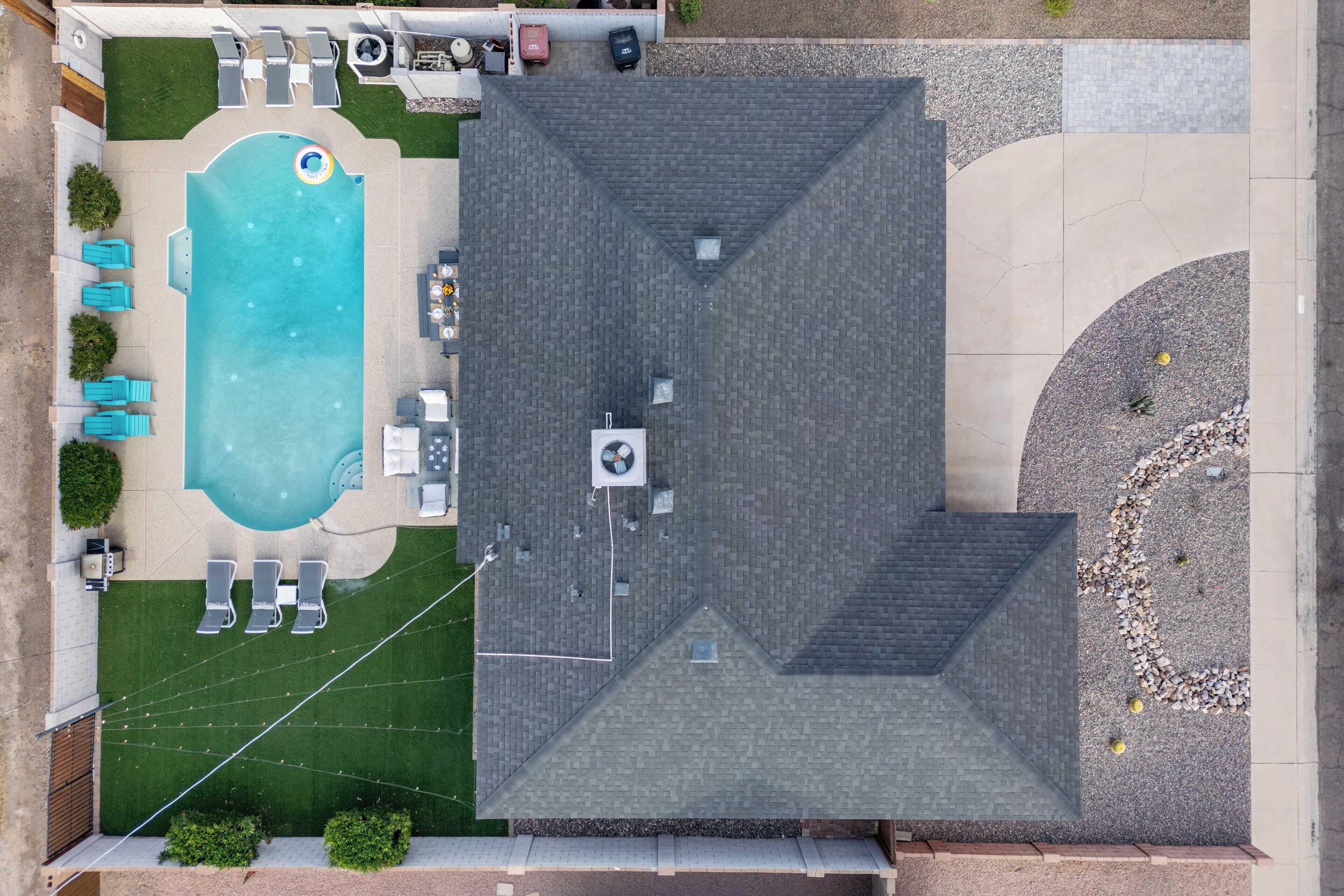 An aerial view of a residential property with a swimming pool, outdoor seating area, and a covered patio.