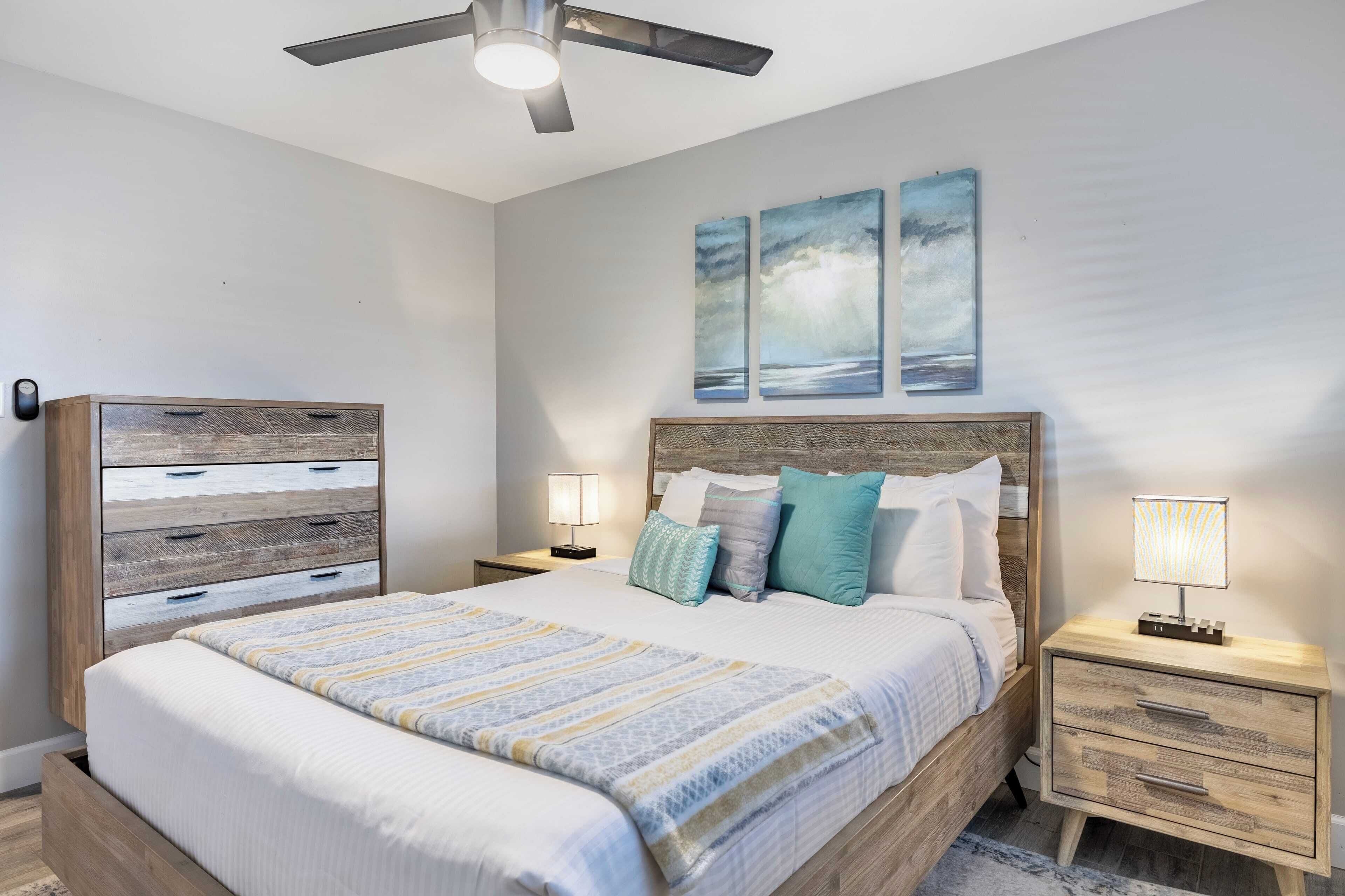 A bedroom with a bed, nightstands, a wooden dresser, and a ceiling fan.