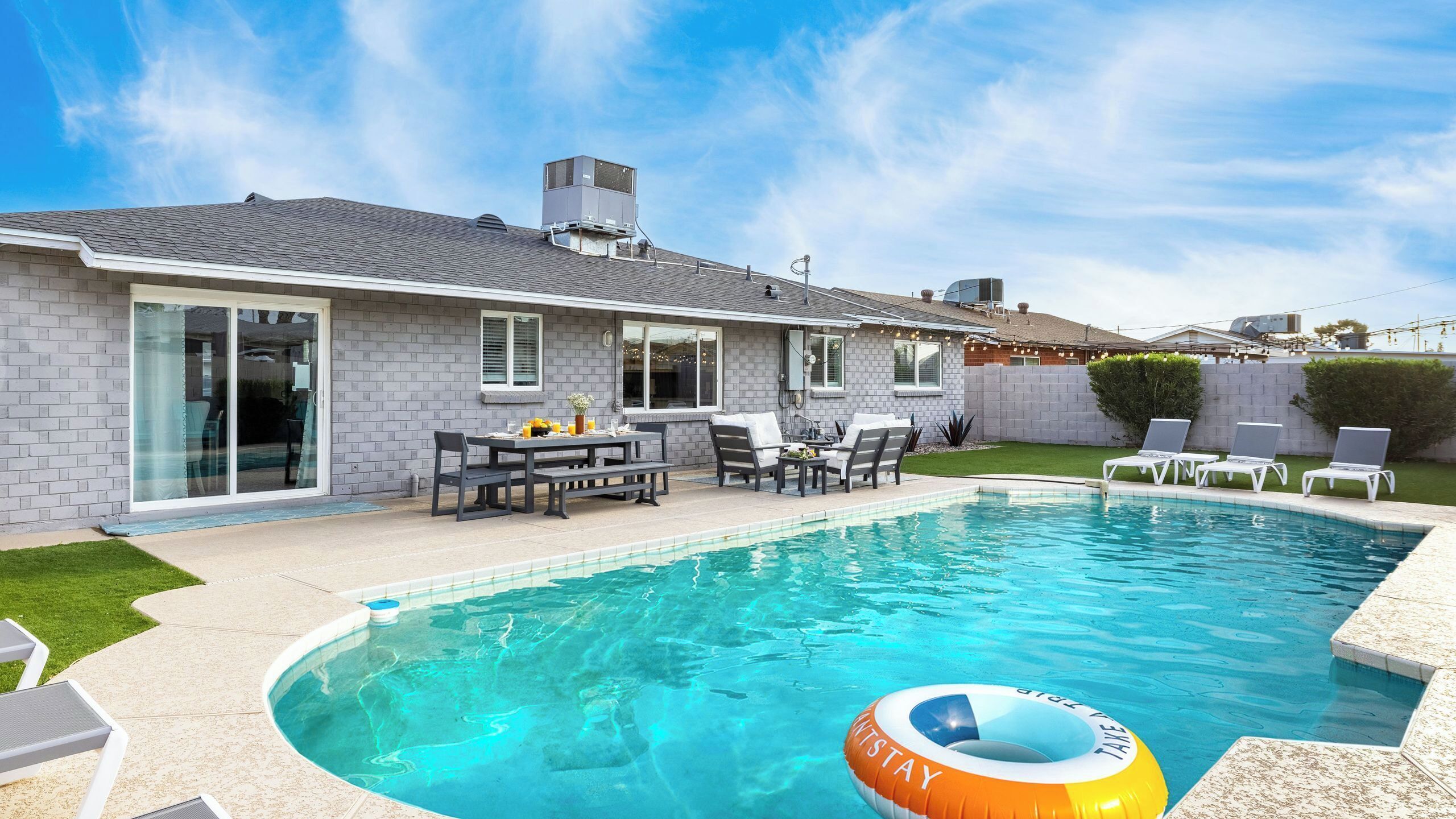 A residential swimming pool with a patio area, a covered outdoor seating area, and a view of the backyard.