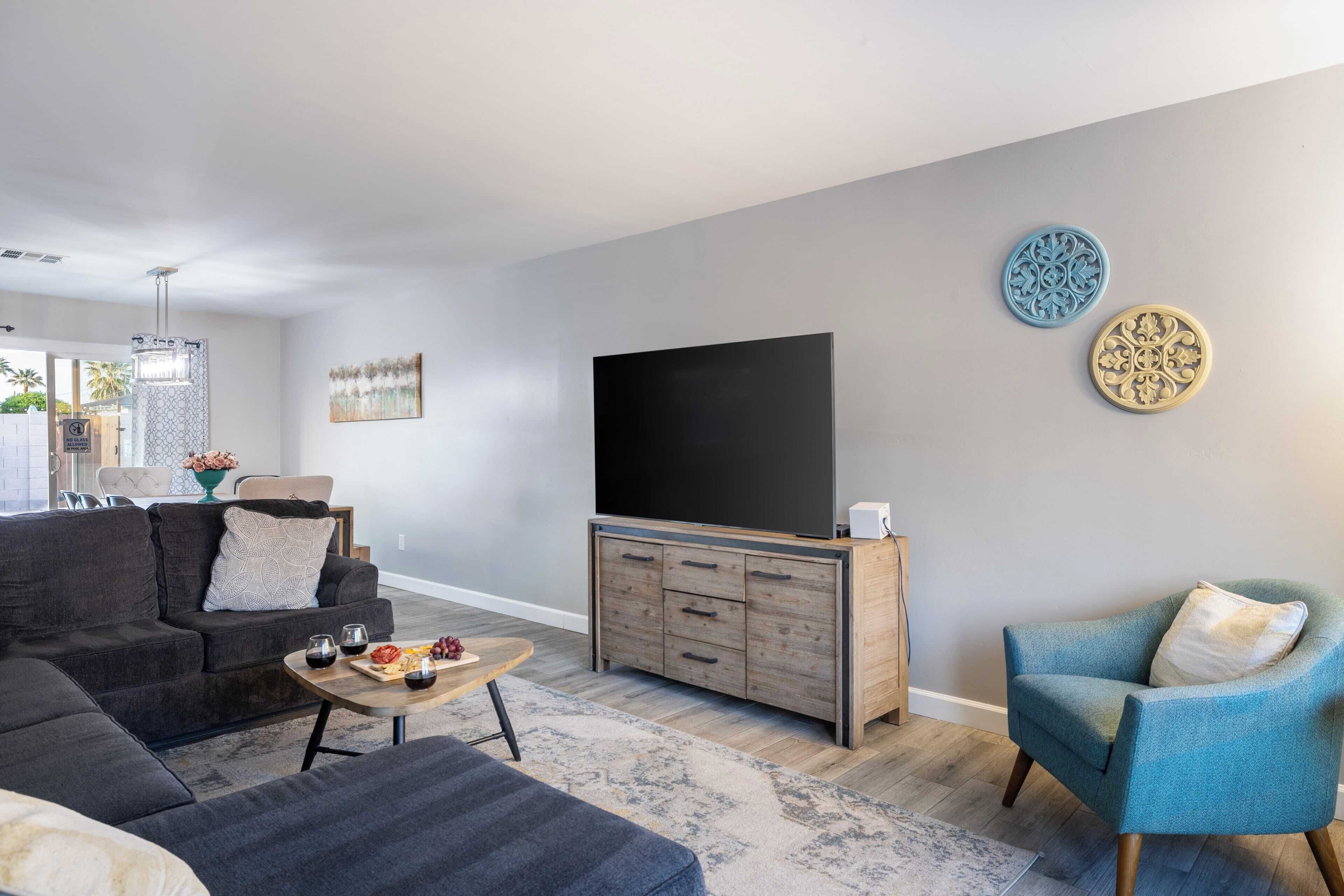 A modern living room with a grey sofa, a blue armchair, a wooden TV stand, and a flat-screen TV.