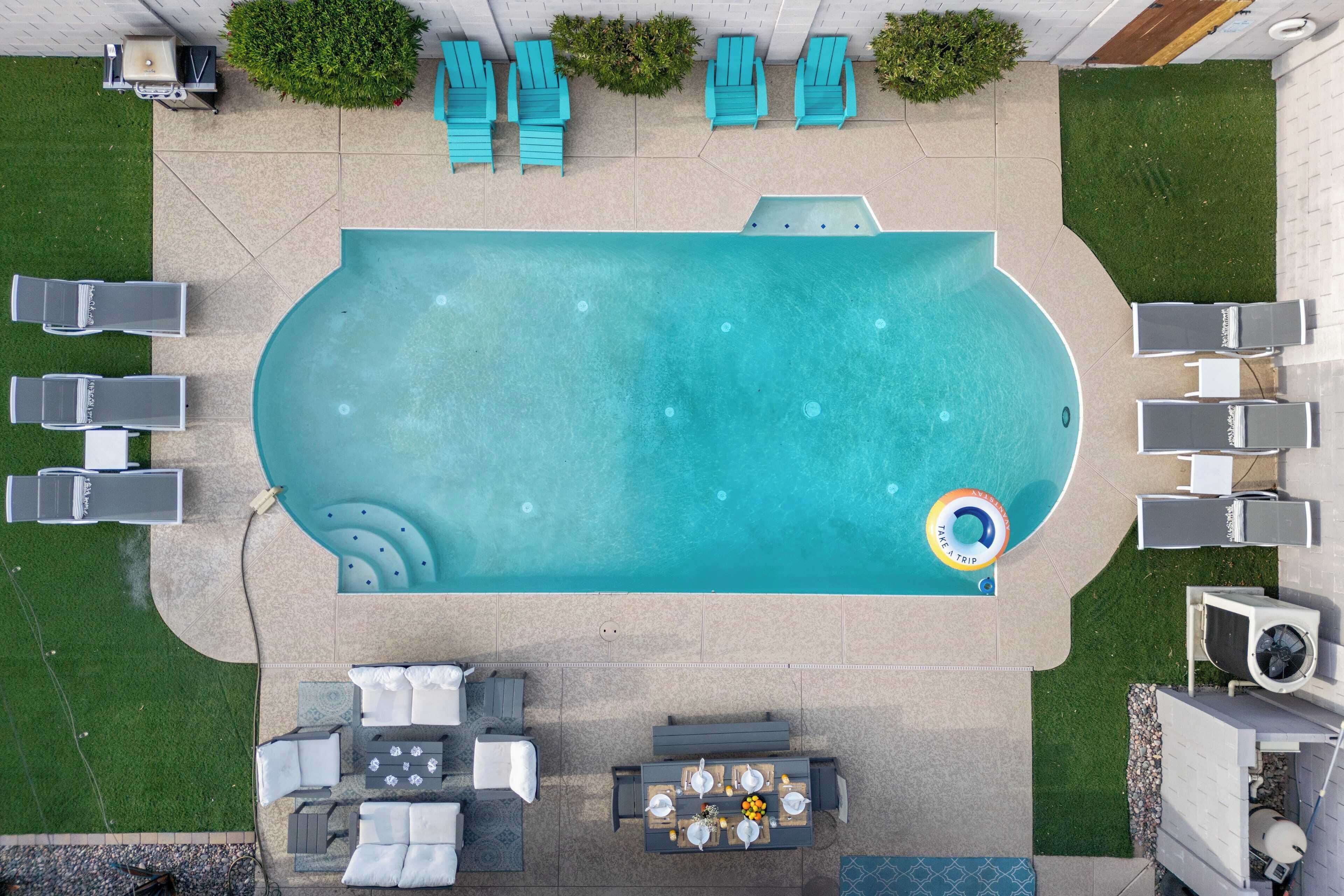 Vue aérienne d’une piscine avec des chaises longues, une table agrémentée d’un arrangement floral et un petit flotteur gonflable.