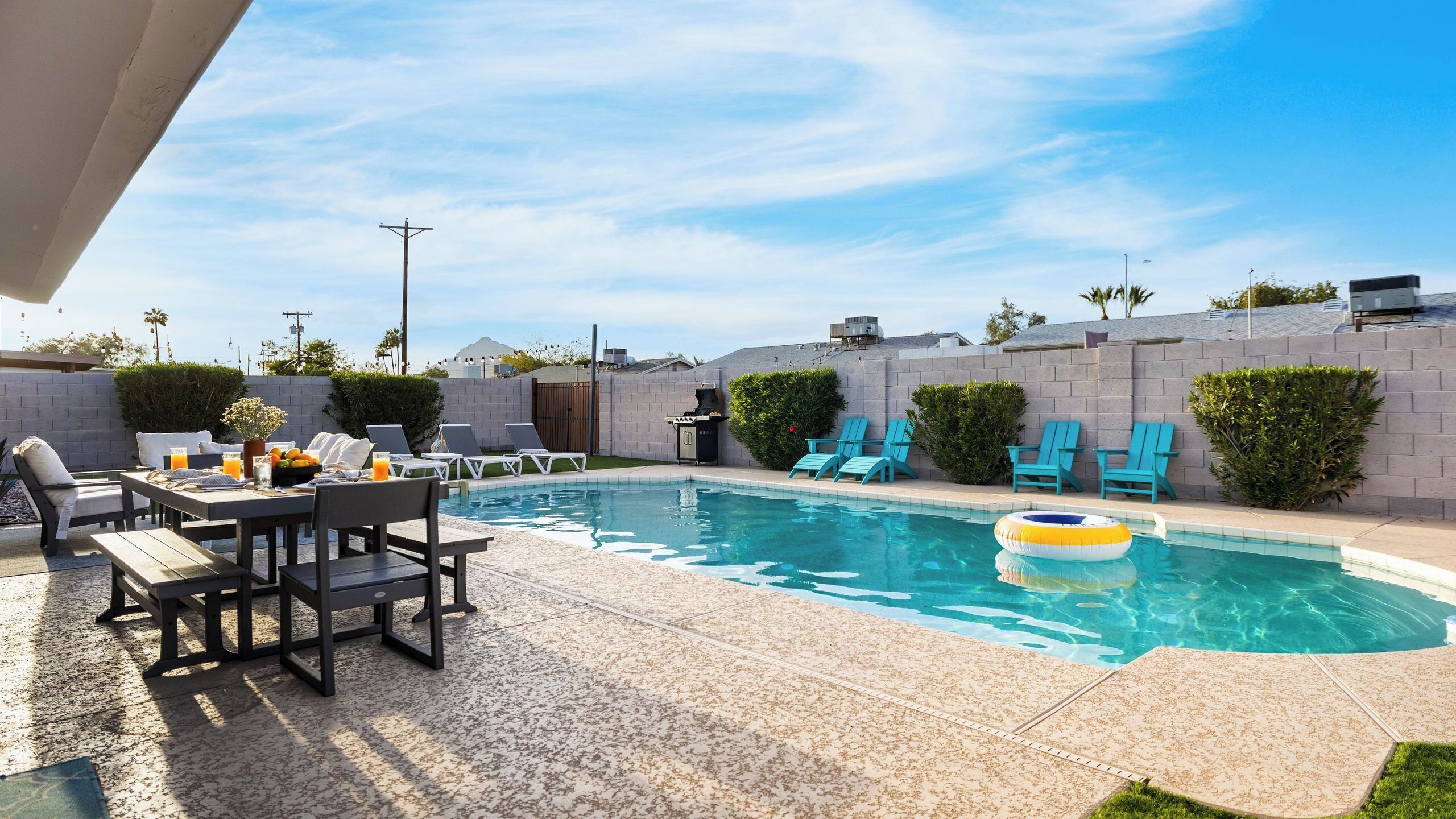 Un patio trasero con piscina, sillas de descanso, una mesa de comedor y una parrilla.