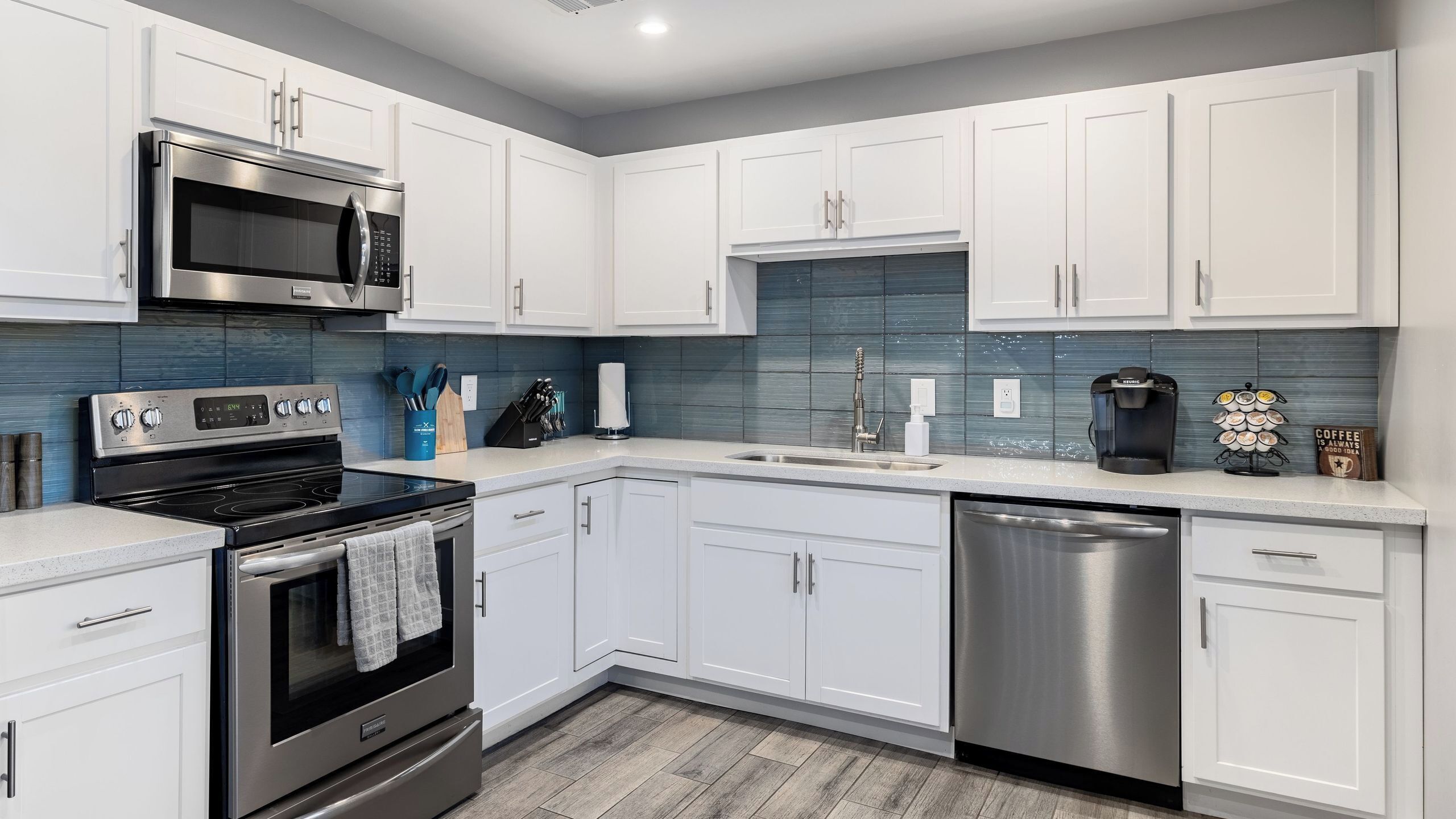 A modern kitchen with white cabinets, stainless steel appliances, and a blue backsplash.