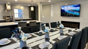 A modern dining area with a long table set for six, surrounded by black chairs. There are floral centerpieces on the table, and a flat-screen TV mounted on the wall above the fireplace. - Private Heated Indoor Pool + No Neighbors + Ski Shawnee/Camelback (East Stroudsburg)