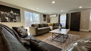 A living room with a sofa, a coffee table, and a cityscape painting on the wall. - Private Heated Indoor Pool + No Neighbors + Ski Shawnee/Camelback (East Stroudsburg)