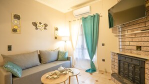 A living room with a sofa, a small round table with decorative items, a fireplace, and a window with curtains. - Corfu Hillside Villa – Terrace, Nature Walks, Sea Views (Agios Martinos)