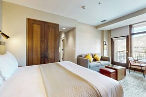 A hotel room with a large bed, a sofa, a desk, and a balcony with a view.