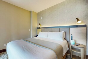 A hotel room with a large bed, a nightstand, and a wall-mounted lamp.