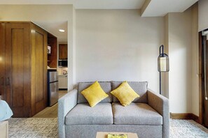 A modern living room with a grey sofa, two yellow cushions, a wooden cabinet, and a kitchen area in the background.