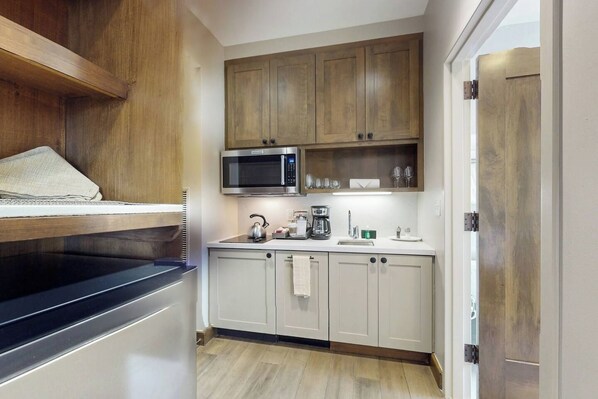A compact kitchen with wooden cabinets, a microwave, a kettle, and a coffee maker.