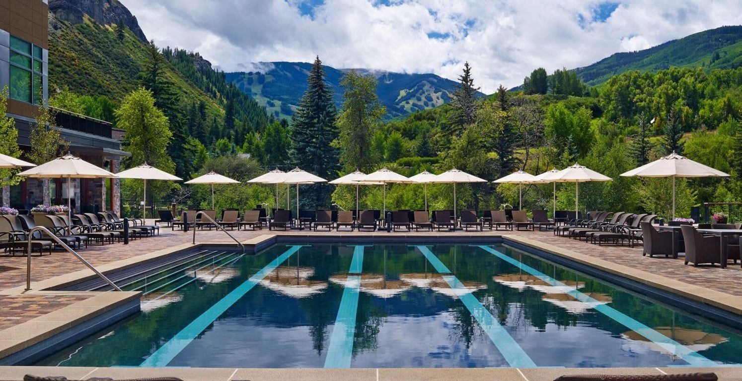 Una piscina con lettini e ombrelloni, circondata da montagne e alberi.