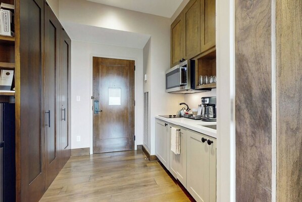 A narrow hallway leading to a kitchen with wooden cabinets, a microwave, and a coffee maker.