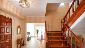 Un escalier en bois avec une rampe, une porte blanche et un couloir menant à une pièce dotée d’une grande fenêtre.