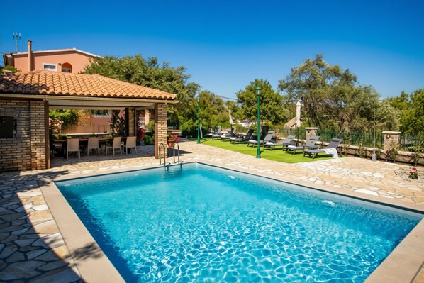 A swimming pool with a stone border, a covered patio area, and lounge chairs.