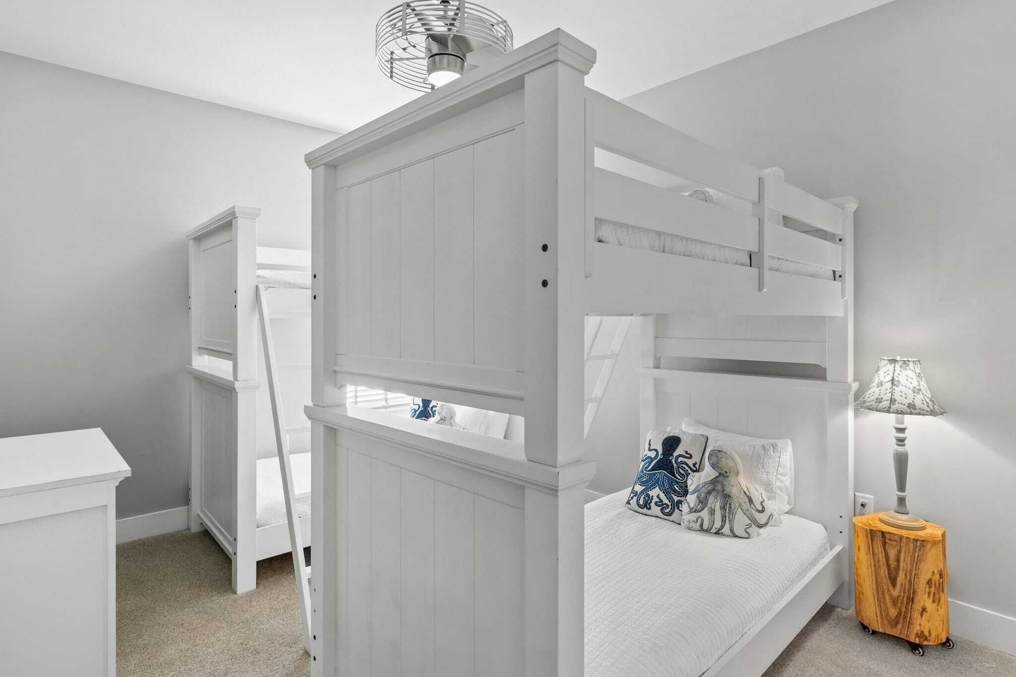 A white bunk bed with a ladder, a bedside table, and a lamp.