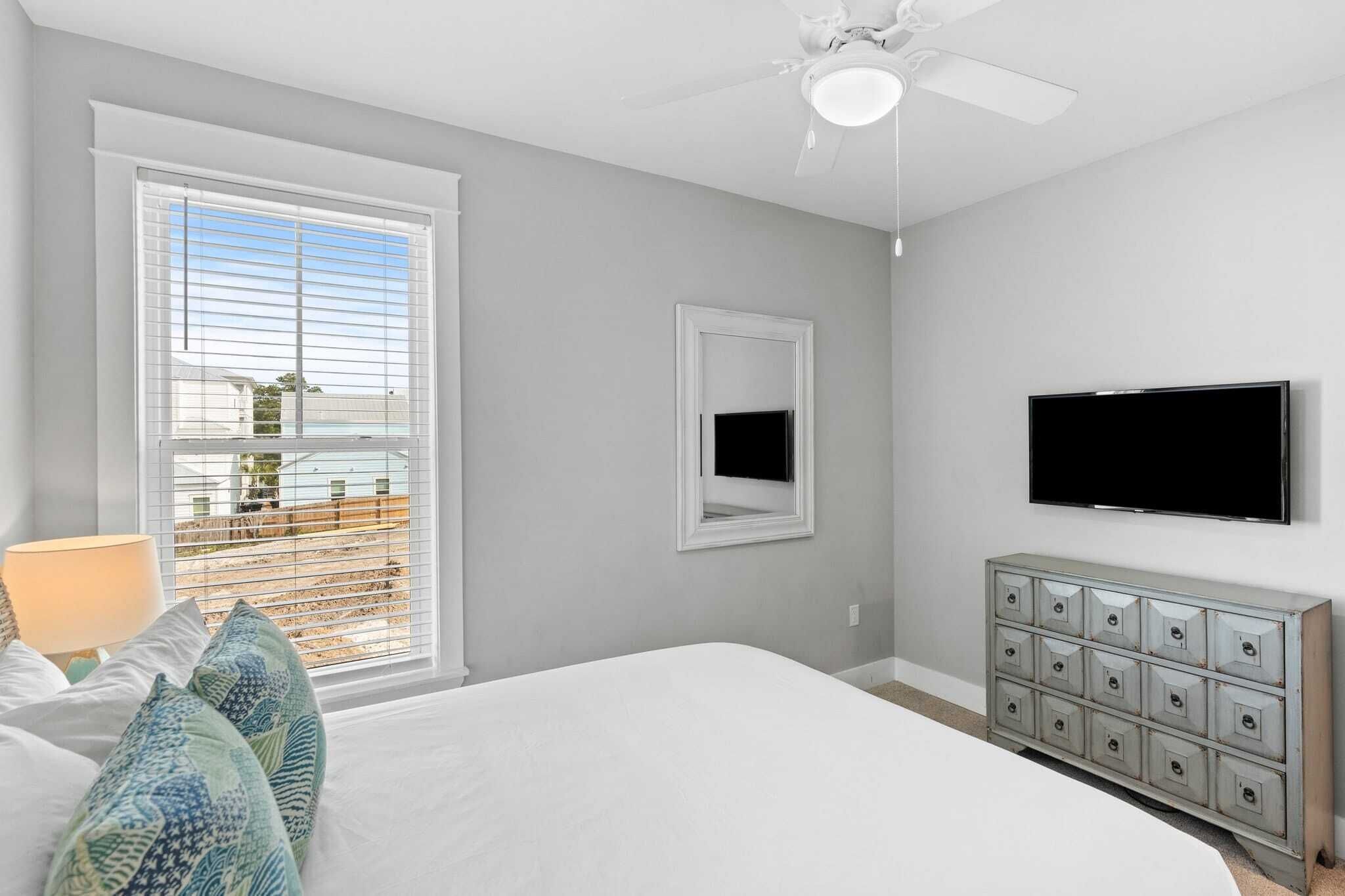 Camera da letto con un letto grande, una ventola a soffitto, una TV a muro e un comò con cassetti.