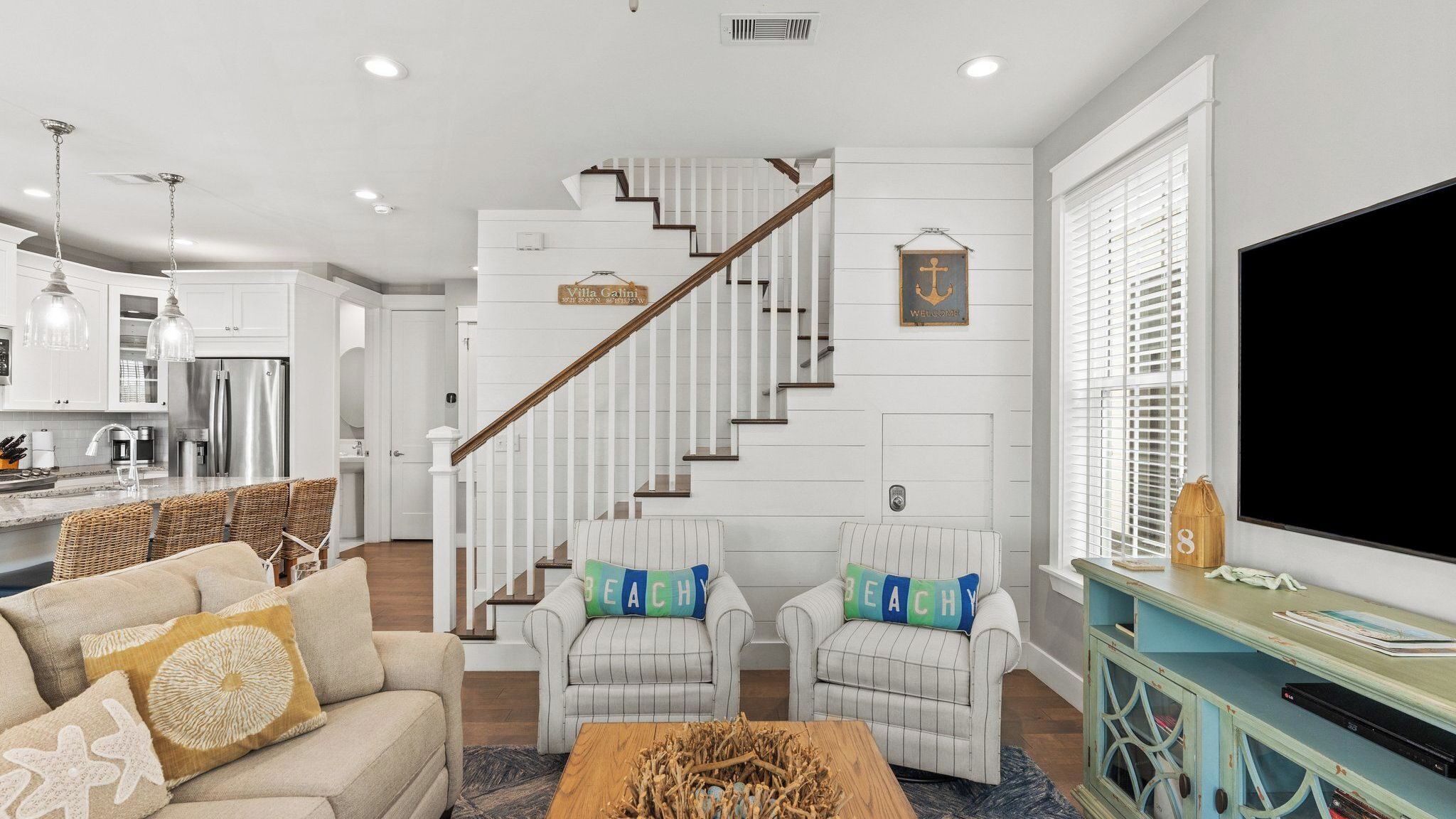 A modern living room with a staircase, a kitchen, and a TV.