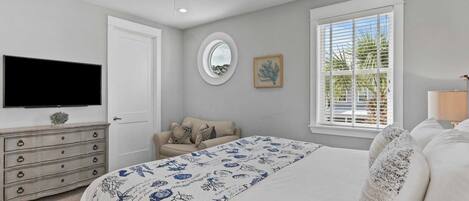 A bedroom with a bed, a dresser, a television, a ceiling fan, a window with blinds, and a framed picture on the wall.