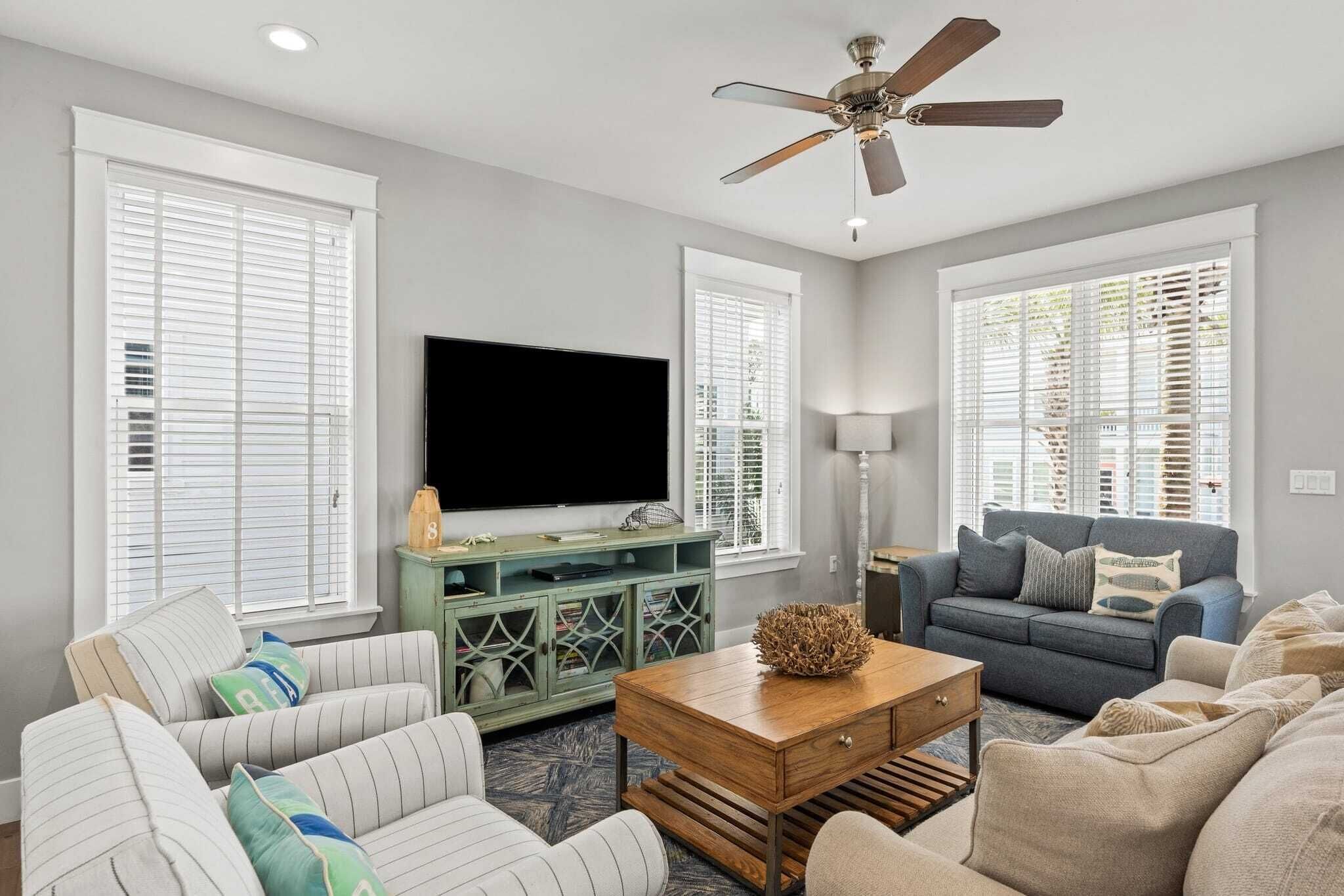 A living room with a flat-screen TV, two sofas, a coffee table, and a ceiling fan.