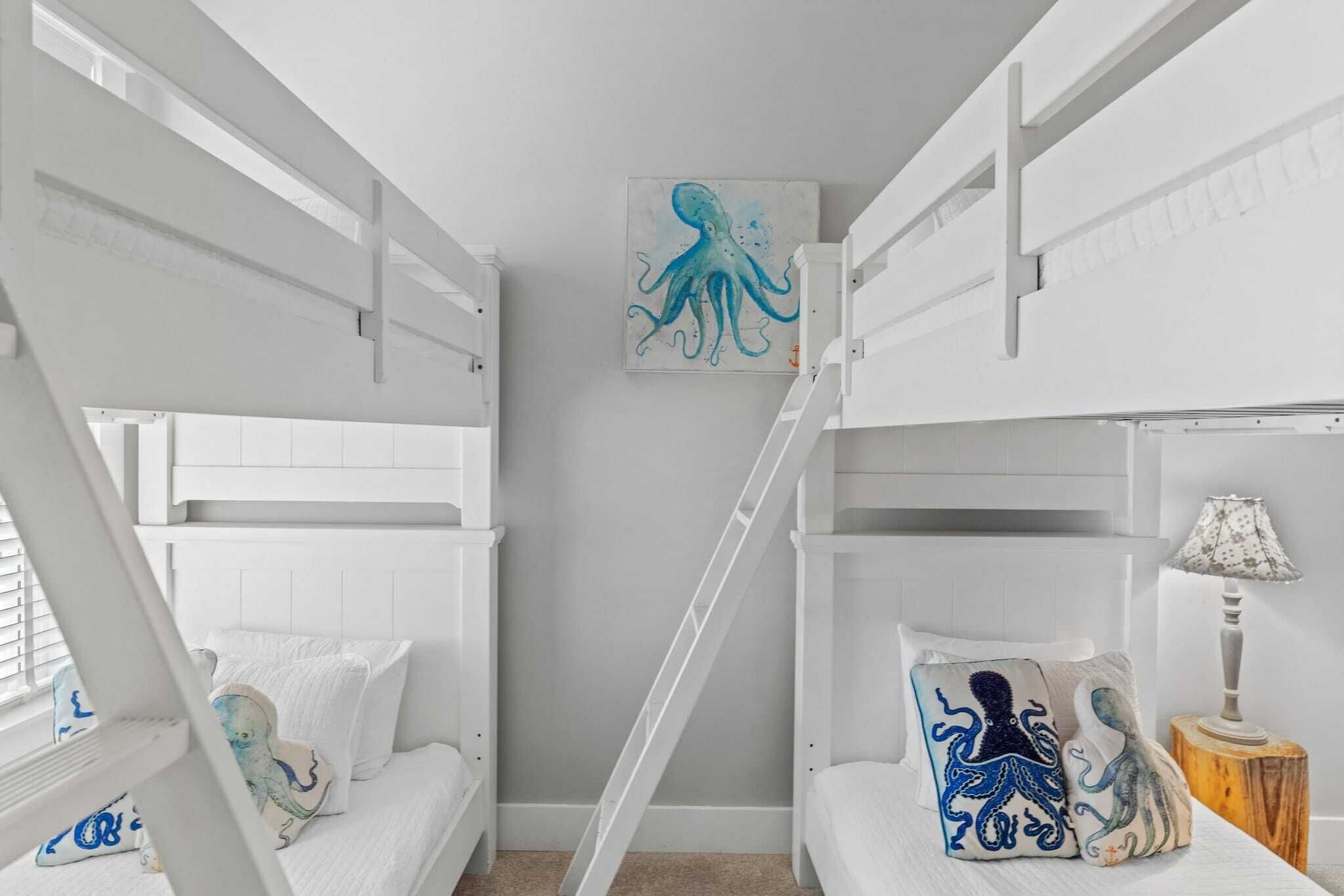 Une chambre avec un lit superposé, du linge de lit blanc, une échelle et un tableau représentant un poulpe sur le mur.
