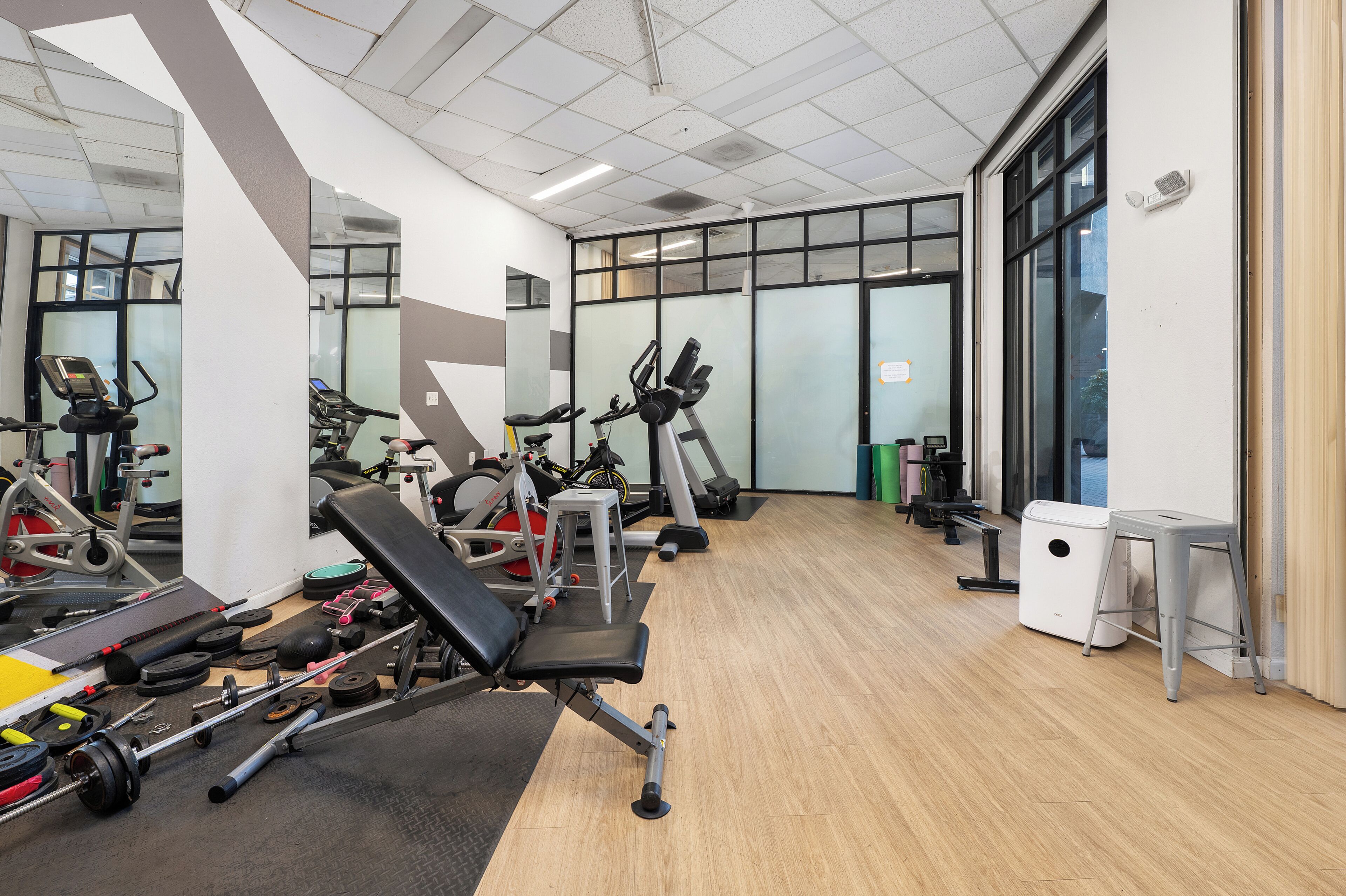 Ein Fitnessraum mit Trainingsgeräten, Spiegeln und Holzboden.
