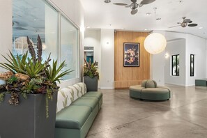 A modern lobby with a green sofa, a wooden accent wall, and a large plant. - Little Italy Inn - Limited Service Apart Hotel (San Diego)