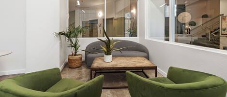 A modern living room with a sofa, two green armchairs, a coffee table, and a potted plant.