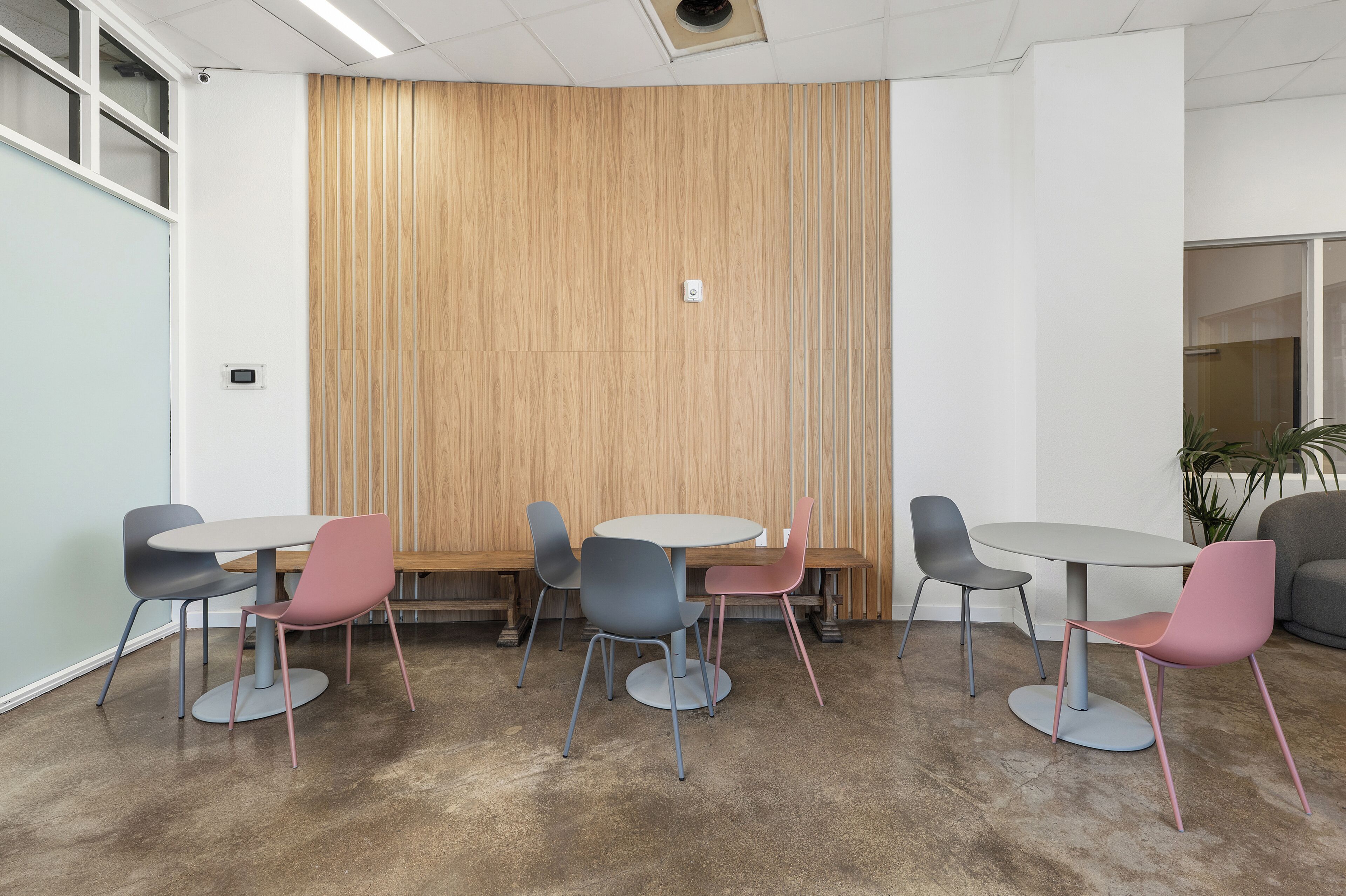 A conference room with a round table, six chairs, a wooden panel wall, and a potted plant.