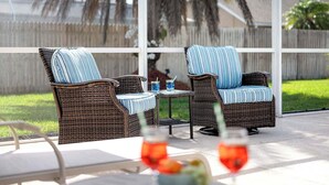 Un patio al aire libre con sillas de mimbre y una mesa, una copa de bebida roja y una copa de bebida azul.