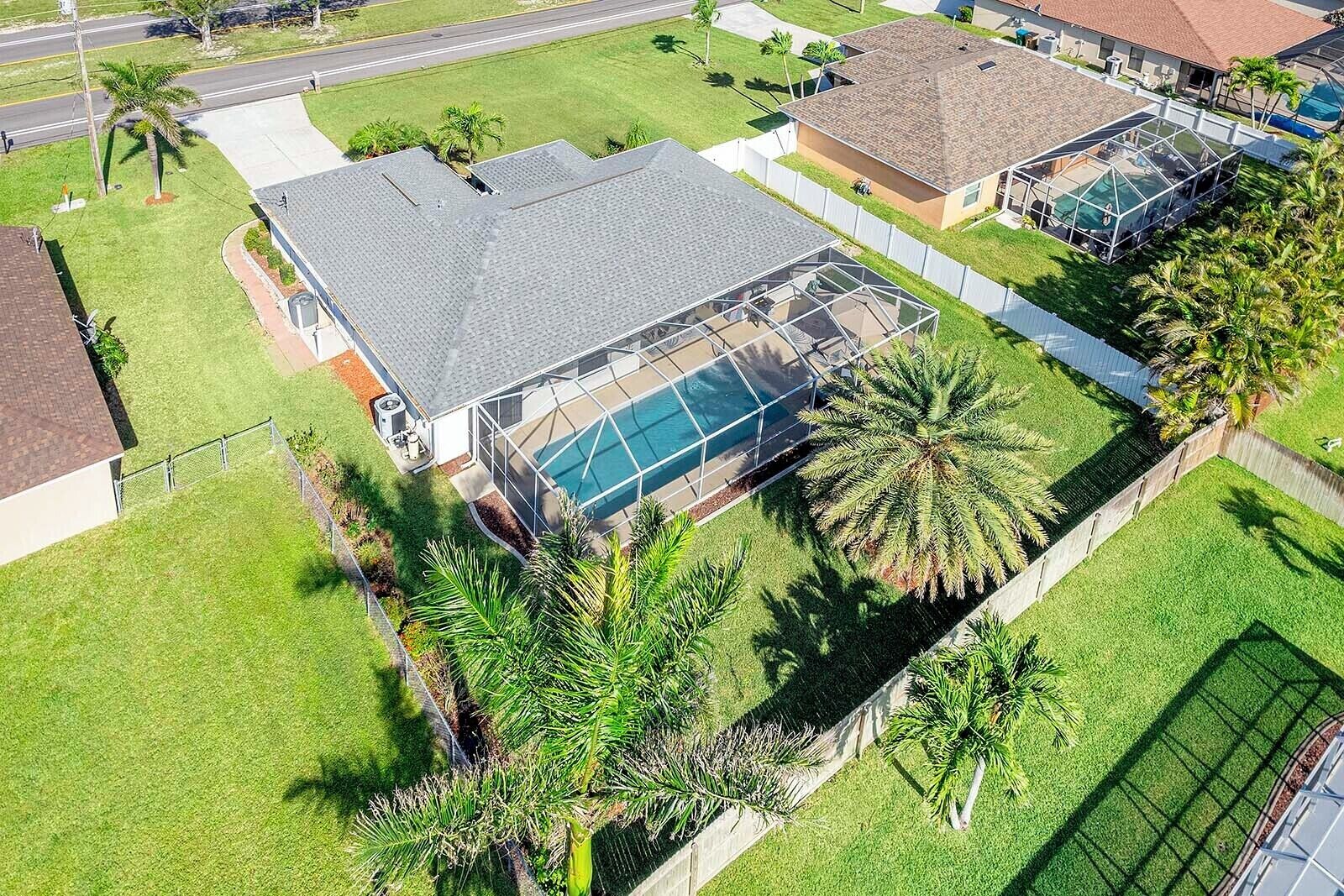 A residential property with a large swimming pool, surrounded by well-maintained lawns and palm trees.
