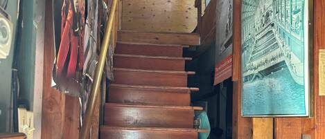 A wooden staircase with a handrail, surrounded by wooden walls and various framed pictures.
