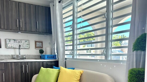 A compact living space with a kitchenette, a sofa with colorful cushions, and a window with blinds. - Startfish #2 Apartment 9 Min to Airport FREE WI-FI (CAROLINA)