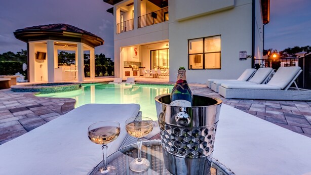 Un espace piscine extérieur moderne, doté d’un jacuzzi, de chaises longues et d’une bouteille de champagne dans un seau en métal.