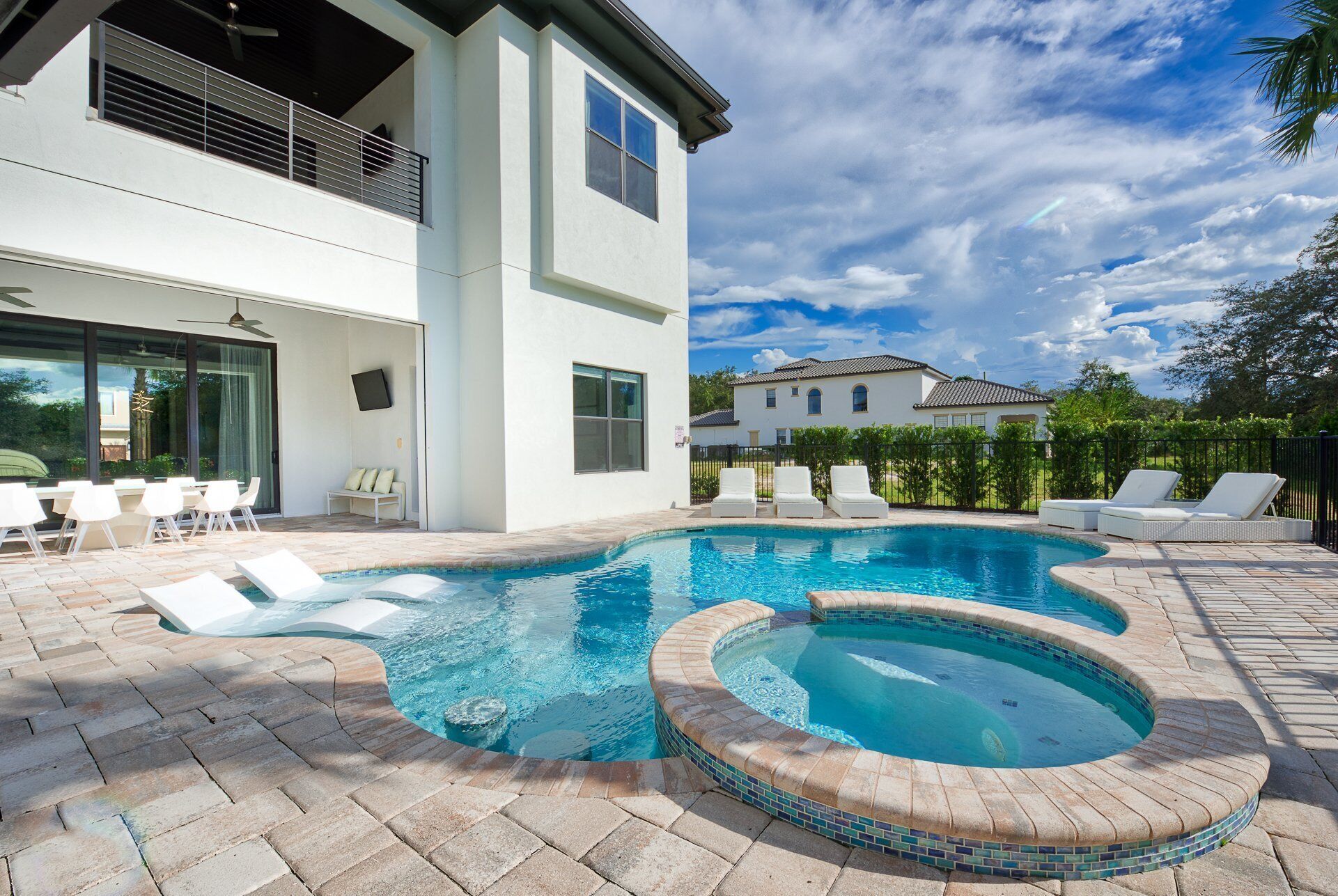 A modern house with a swimming pool, a patio with lounge chairs, and a view of another house in the background.