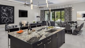 Une cuisine moderne dotée d’un plan de travail en marbre, de meubles de rangement noirs et de luminaires suspendus.