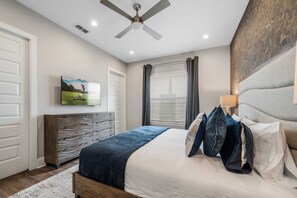 A bedroom with a bed, a ceiling fan, a TV mounted on the wall, and a window with curtains.