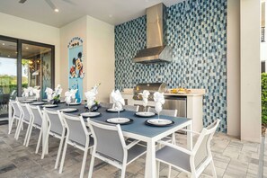 A dining area with a long table set for a meal, a grill, and a Mickey Mouse mural on the wall.