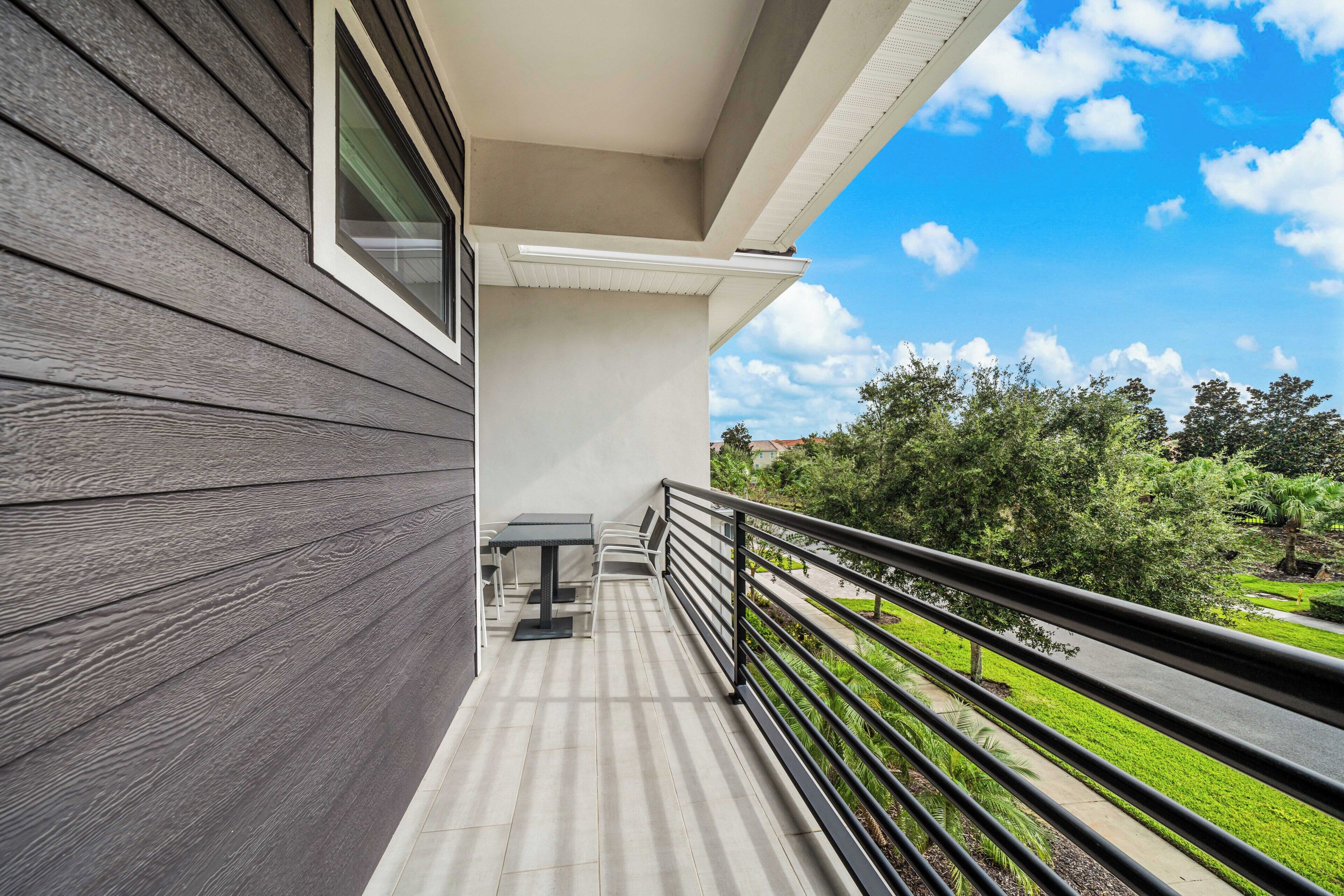 A balcony with a table and chairs, a railing, and a view of greenery and buildings.
