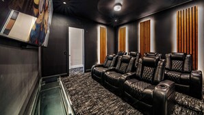 A home theater room with a large screen, reclining leather chairs, and a carpeted floor.