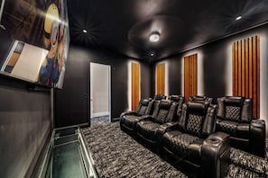 Una sala de cine en casa con una pantalla grande, sillones de cuero reclinables y piso alfombrado.